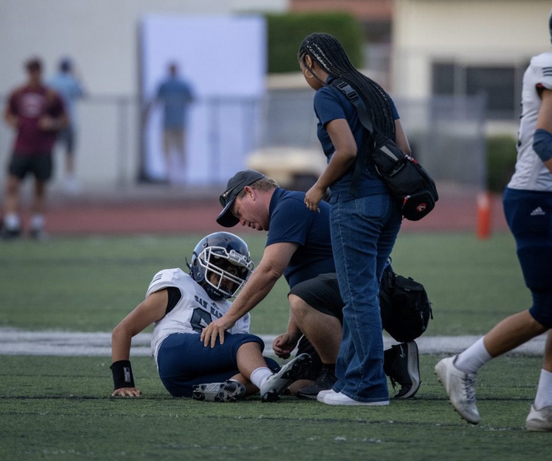 Trainer helping collapsed football player on the field. Image taken by @csharshotos on Instagram.